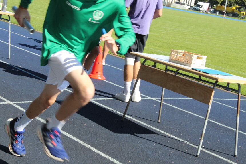 Foto: Sportler rennt mit Staffelstab über die Tartanbahn.