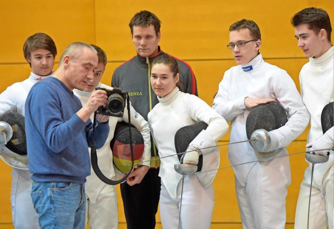 Nahaufnahme: Peter Endig zeigt den Fechtern Julius Michalski, Niclas Helbig, Trainer Jörg Fiedler, Klara Jaskulla, Jonas Enzmann und Artur Fischer (v. l.) verschiedene Motive fürs WM-Plakat.
